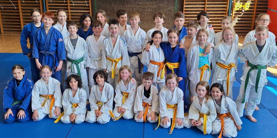Gruppe von Kindern in wei&szlig;en und blauen Judokas, auf einer Judo-Matte stehend, in einer Sporthalle.