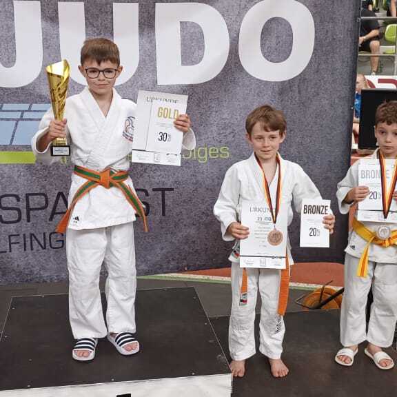 Sechs Kinder stehen auf dem Siegertreppchen eines Judoturniers, einer h&auml;lt einen Pokal und Urkunden.
