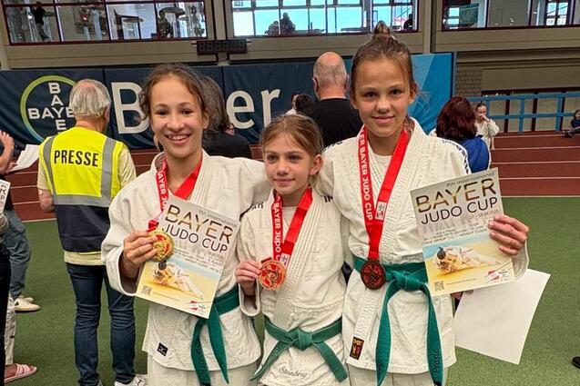 Drei junge Judoka in wei&szlig;en Anz&uuml;gen mit Medaillen und Urkunden beim Bayer Judo Cup auf einer Sportfl&auml;che.