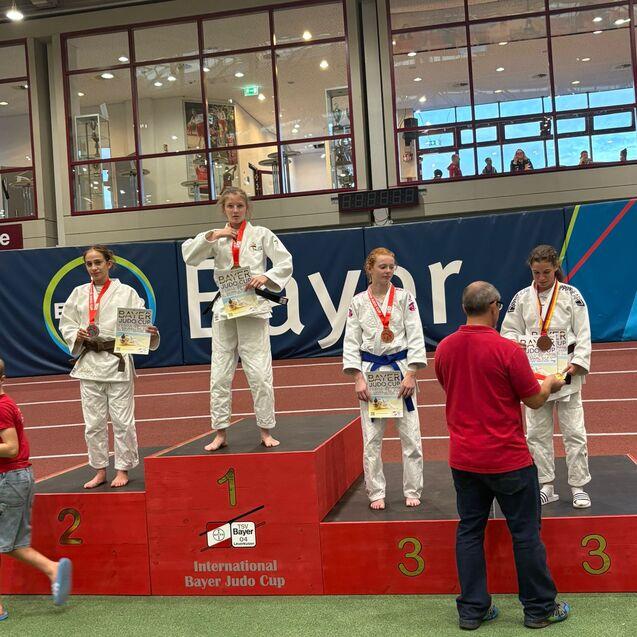 Vier Judokas in wei&szlig;en Anz&uuml;gen stehen auf dem Siegerpodest beim Bayer Judo Cup, jeder mit Medaille und Urkunde.