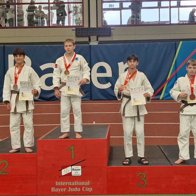 F&uuml;nf Judokas auf einem Podest beim Bayer-Judo-Cup, Medaillen um den Hals, Urkunden in der Hand.