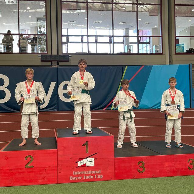 Junge Judoka stehen auf dem Siegerpodest beim Internationalen Bayer Judo Cup, mit Medaillen und Urkunden in der Hand.
