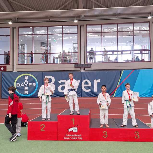 Junge Judoka stehen stolz auf dem Siegertreppchen des Internationalen Bayer Judo Cups mit Medaillen.