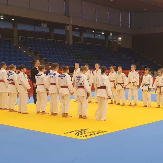 Anordnung von Judokas in wei&szlig;en Anz&uuml;gen auf einer blauen und gelben Matte in einer Sporthalle w&auml;hrend eines Wettkampfs.