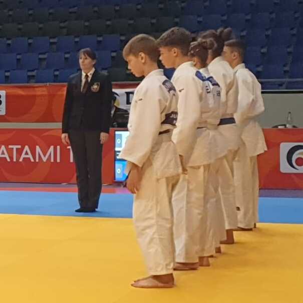 Zwei Mannschaften in Judoanz&uuml;gen stehen sich auf einer Judomatte gegen&uuml;ber, bereit zum Wettkampf.
