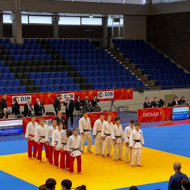 Gruppe von Judoka in wei&szlig;en und roten Anz&uuml;gen steht auf einer Judomatte w&auml;hrend eines Wettkampfs.