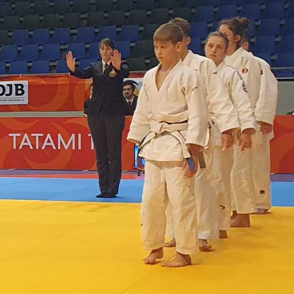 Zwei Gruppen von Judokas in wei&szlig;em und gr&uuml;nem Gi stehen auf einer Matte bei einem Wettkampf.