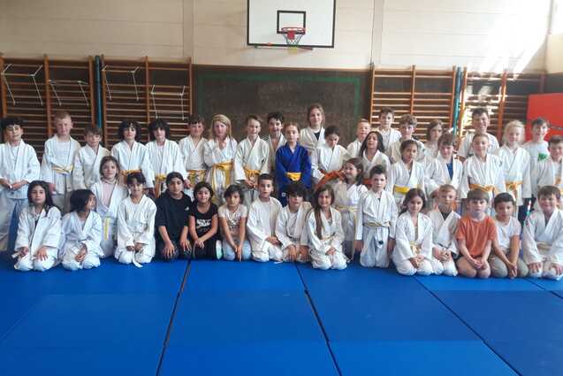 Gruppenfoto von Kindern in wei&szlig;en Judogis auf einer blauen Judomatte in einer Sporthalle.