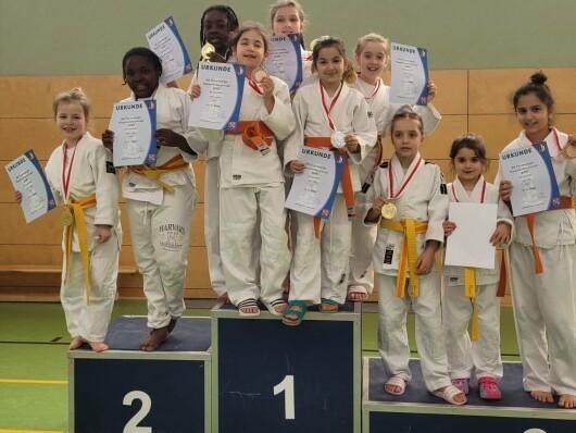 Gruppenzusammenhalt von Mädchen in Judoanzügen, die stolz Urkunden und Medaillen auf einem Siegertreppchen zeigen.