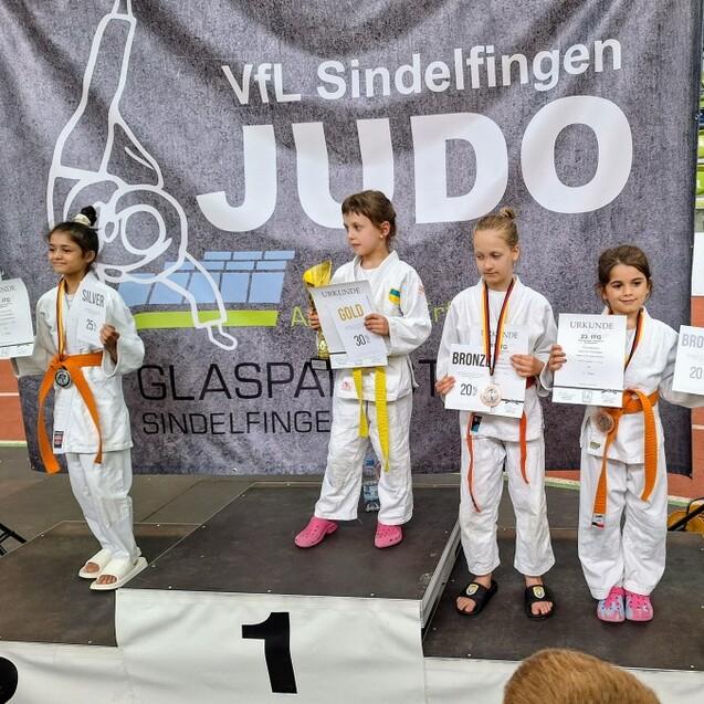 Sieben Kinder in Judogis stehen auf dem Siegerpodest und halten ihre Urkunden und Medaillen bei einem Judo-Wettkampf.