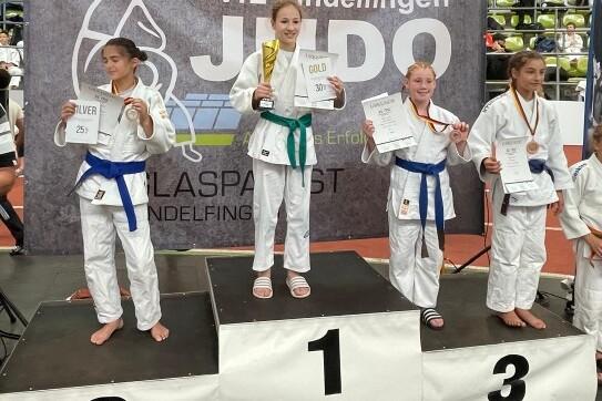 Siegerinnen des Judo-Turniers stehen auf dem Podium, pr&auml;sentieren Urkunden und Medaillen vor einer Veranstaltungswand.