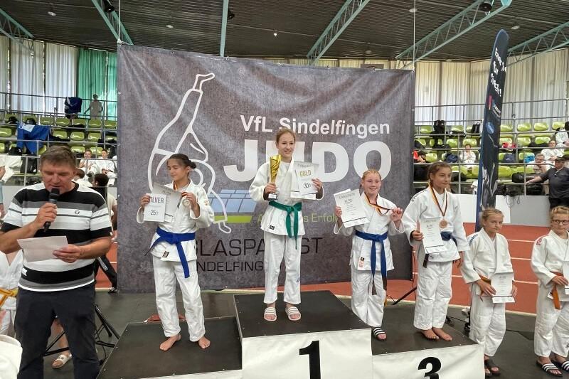 Siegerinnen des Judo-Turniers stehen auf dem Podium, pr&auml;sentieren Urkunden und Medaillen vor einer Veranstaltungswand.
