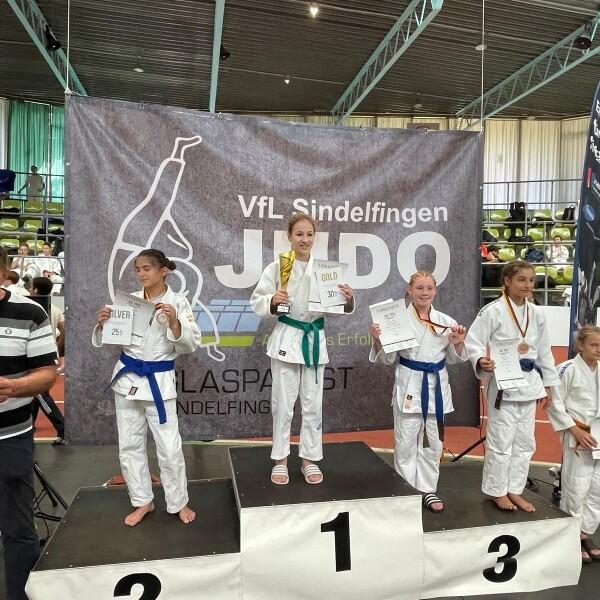 Siegerinnen des Judo-Turniers stehen auf dem Podium, pr&auml;sentieren Urkunden und Medaillen vor einer Veranstaltungswand.