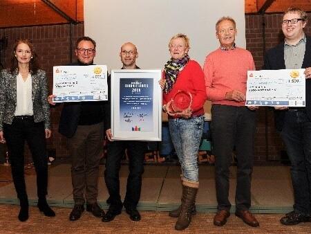 Fünf Personen stehen zusammen und halten Urkunden und einen Preis in einer festlichen Umgebung.