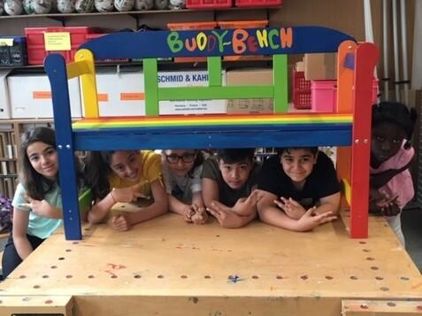 Sechs Kinder posieren unter einer bunten Buddy-Bank auf einem Tisch in einem Klassenraum.