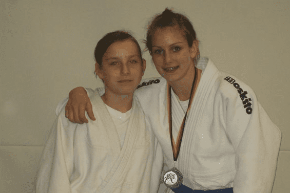 Zwei junge Judoka in weißen Judogis stehen nebeneinander, eine trägt eine Medaille und zeigt stolz ihr Lächeln.