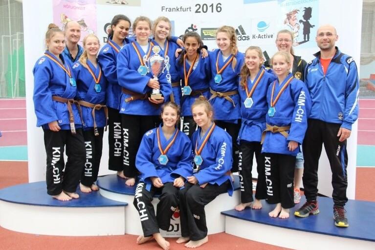 Gruppe junger Sportlerinnen in blauen Anzügen mit Pokal und Medaillen auf dem Siegerpodest, Frankfurt 2016.