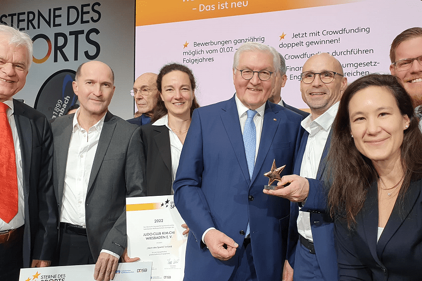 Gruppendynamik bei einer Preisverleihung: Personen halten Pokal, Urkunden und posieren lächelnd vor einer Präsentation.