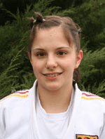 Porträt eines jungen Mädchens in einem weißen Judoanzug vor grüner Vegetation. Sie lächelt freundlich in die Kamera.