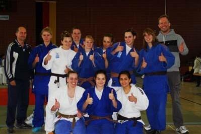 Gruppennahaufnahme von Judo-Athletinnen in blauen und weißen Judogis, die lächeln und Daumen hoch zeigen.
