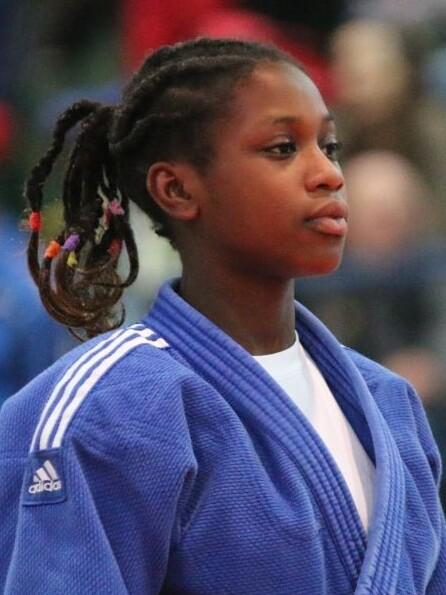 Junge Judo-K&auml;mpferin in blauer Judokleidung, vorbereitet f&uuml;r einen Wettkampf in einer Halle voller Zuschauer.