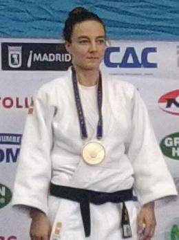 Vier Judoka stehen auf dem Siegerpodest, drei mit Medaillen, vor einer Bannerwand in einer Sporthalle.