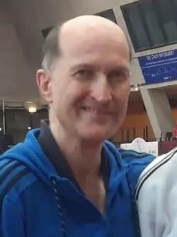 Ein junger Judoka in weißem Gi mit Medaille steht neben einem Trainer in blauer Jacke auf einer Judomatte.