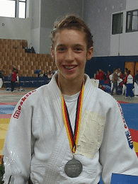 Junger Judoka mit Silbermedaille, Blumenstrau&szlig; und Urkunde in einer Sporthalle.
