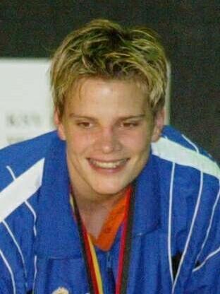 L&auml;chelnder junger Sportler in blauer Jacke, h&auml;lt eine Rose und zeigt eine Goldmedaille.