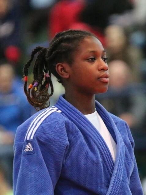 Junge Judo-K&auml;mpferin in blauer Judokleidung, vorbereitet f&uuml;r einen Wettkampf in einer Halle voller Zuschauer.
