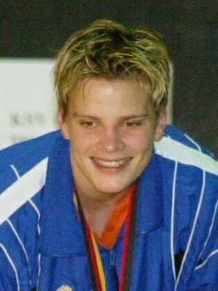 L&auml;chelnder junger Sportler in blauer Jacke, h&auml;lt eine Rose und zeigt eine Goldmedaille.