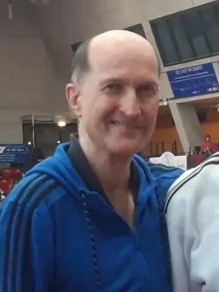 Ein junger Judoka in wei&szlig;em Gi mit Medaille steht neben einem Trainer in blauer Jacke auf einer Judomatte.