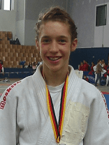 Junger Judoka mit Silbermedaille, Blumenstrauß und Urkunde in einer Sporthalle.