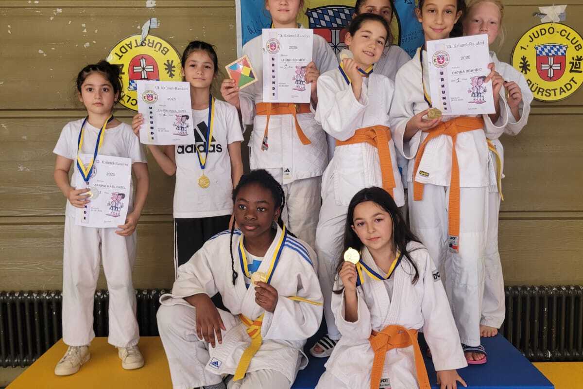 Gruppenfoto von sieben jungen Judokas in wei&szlig;en Anz&uuml;gen mit Medaillen und Urkunden auf bunten Wettkampfb&ouml;den.