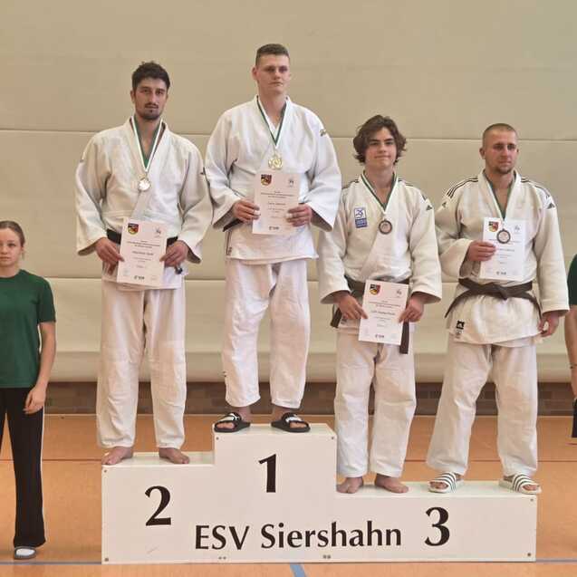 Sieben Personen stehen auf dem Siegerpodest einer Sportveranstaltung, drei in Judoanz&uuml;gen mit Medaillen.