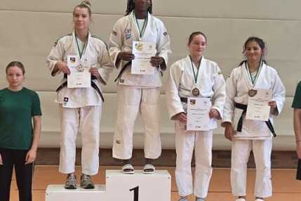 Sieben Sportler stehen auf dem Treppchen, wobei der erste Platz oben mit einer Medaille ausgezeichnet ist.