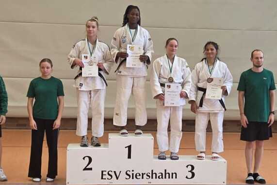 Sieben Sportler stehen auf dem Treppchen, wobei der erste Platz oben mit einer Medaille ausgezeichnet ist.