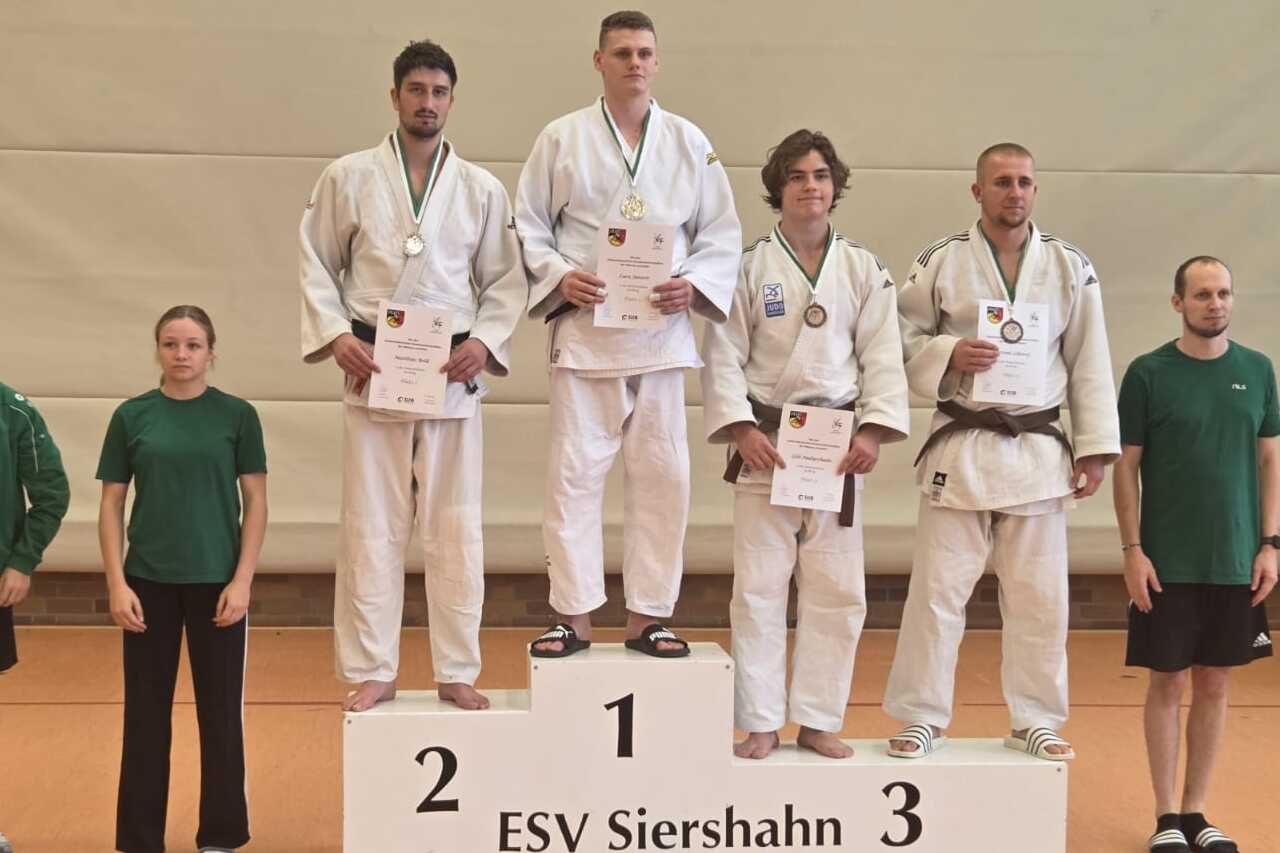 Sieben Personen stehen auf dem Siegerpodest einer Sportveranstaltung, drei in Judoanzügen mit Medaillen.