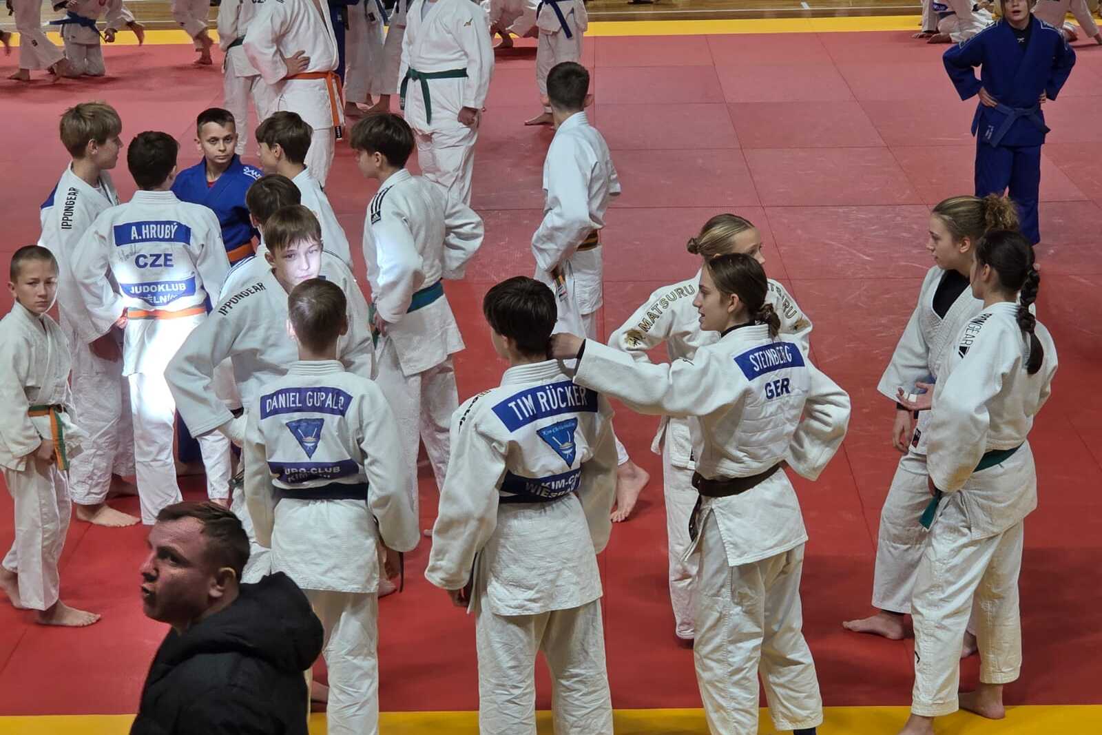 Junge Judoka in weißen Gi stehen auf einer roten Matte und unterhalten sich vor dem Training.