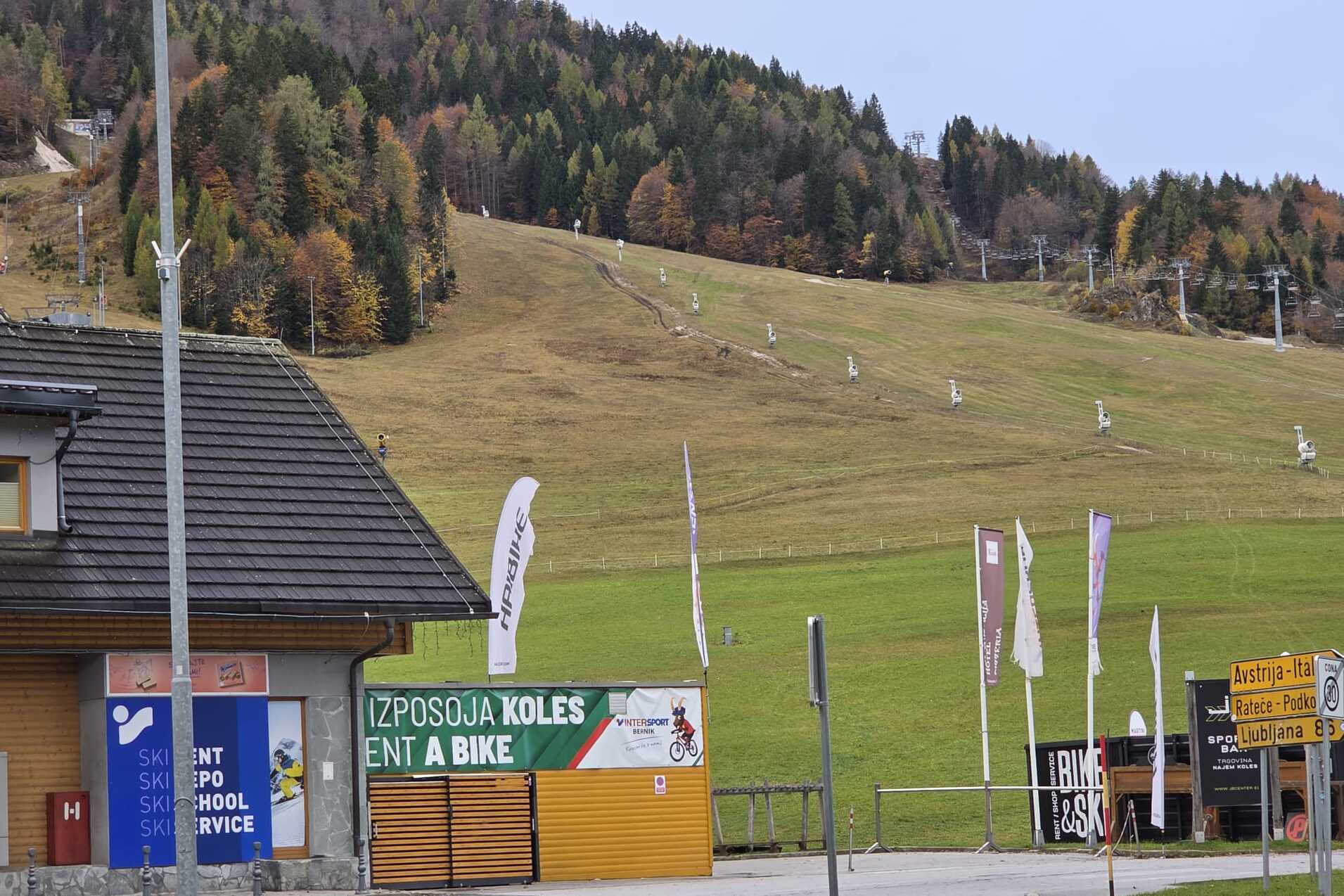 Blick auf eine Wiese mit Skiliften im Hintergrund und einem Mietservice f&uuml;r Fahrr&auml;der im Vordergrund.