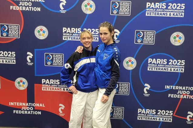 Zwei Judokas in Wettbekleidung posieren vor einem Banner der Paris World Judo Championships 2025.