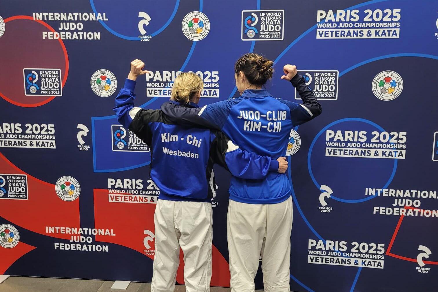 Zwei Judokas mit R&uuml;ckansicht posieren vor einem Banner der Paris World Judo Championships 2025.