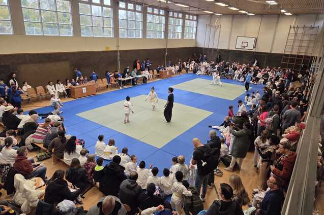 Judo-Wettkampf in einer Sporthalle mit Zuschauern und Athleten auf blauen Matten.