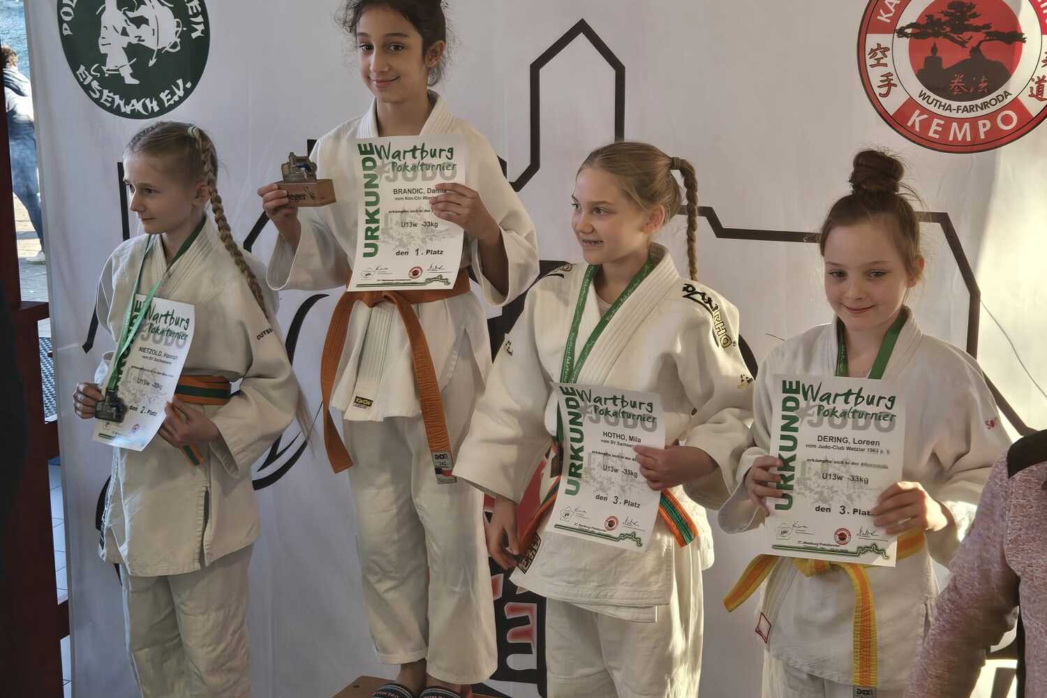 Vier Kinder in Judokleidung stehen auf einem Siegertreppchen und halten Urkunden und Medaillen in den Händen.