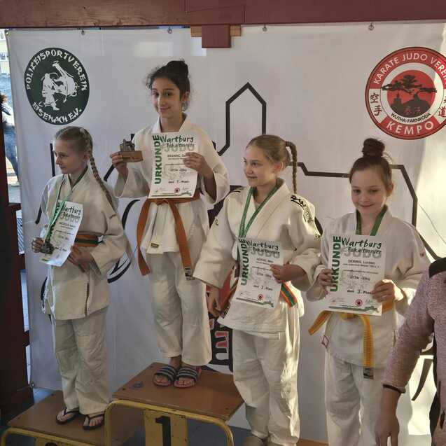 Vier Kinder in Judokleidung stehen auf einem Siegertreppchen und halten Urkunden und Medaillen in den H&auml;nden.