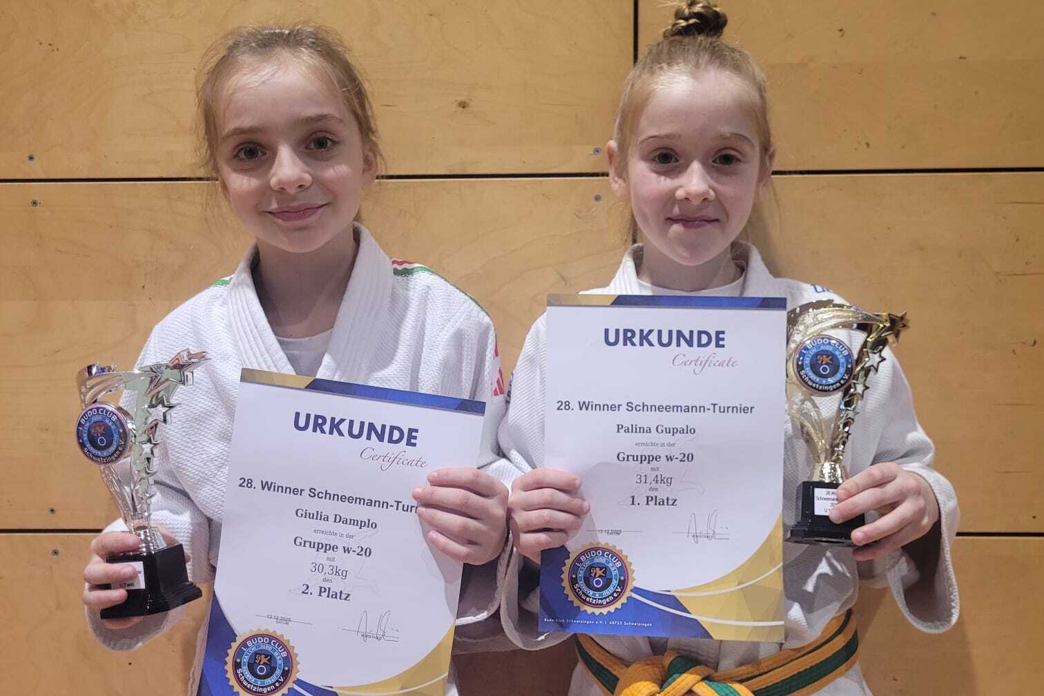 Zwei Kinder in Karateanzügen halten Pokale und Urkunden für den zweiten Platz bei einem Wettkampf.