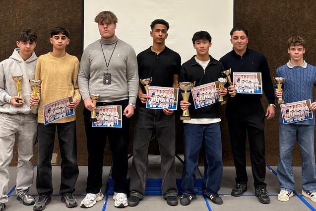 Gruppe von sieben Jugendlichen mit Pokalen und Urkunden vor einer Leinwand in einem Veranstaltungsraum.