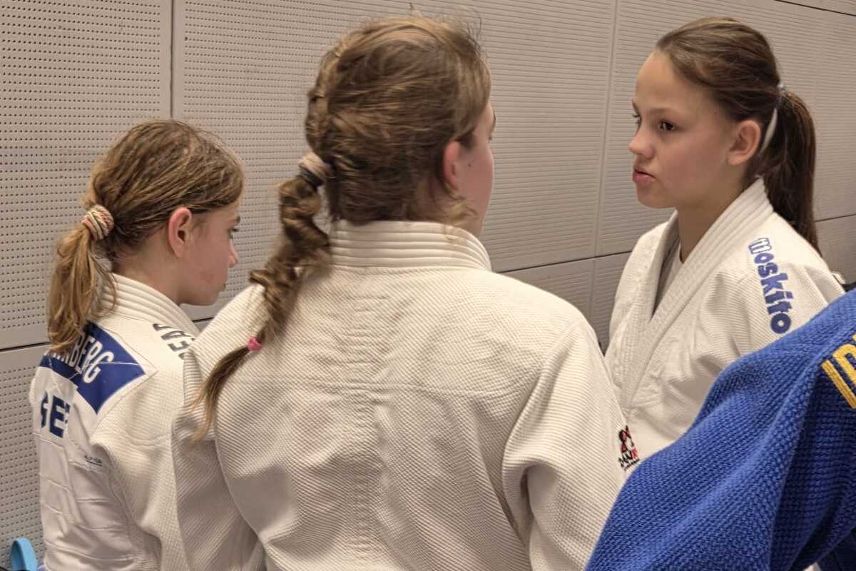 Drei Judoka in weißen Anzügen stehen zusammen, eine trägt einen blauen Gürtel, während sie sich unterhalten.