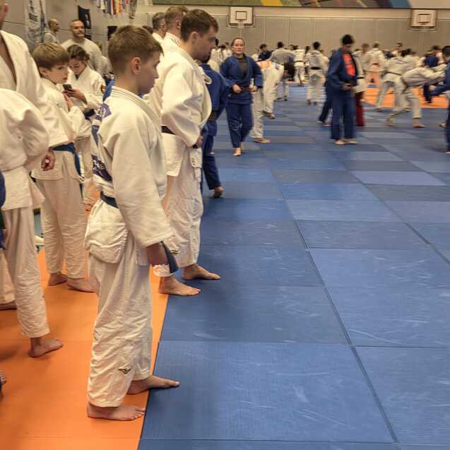 Gruppe von Judokas in wei&szlig;en und blauen Gis, die auf blauen Matten in einer Halle stehen und sich auf das Training vorbereiten.