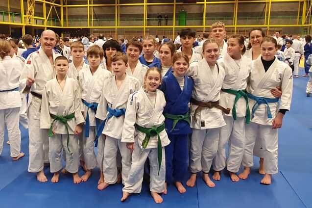 Gruppensicht von Judoka in wei&szlig;en und blauen Kimonos auf einer blauen Matte in einer Turnhalle.
